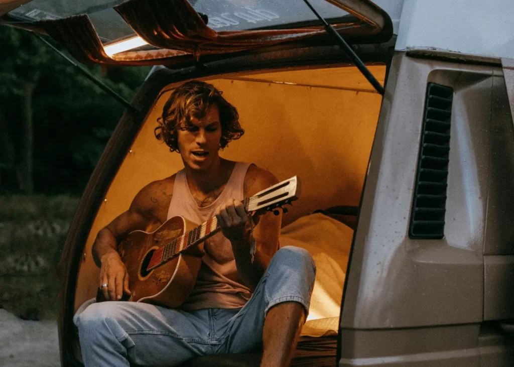 Man Playing Acoustic Guitar While Sitting on a Van