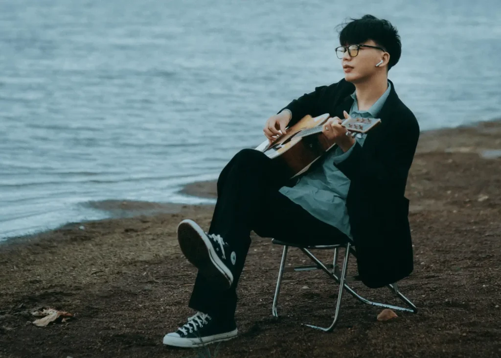 Man Sitting on a Chair on a Beach Playing his Guitar. guitar captions for Instagram