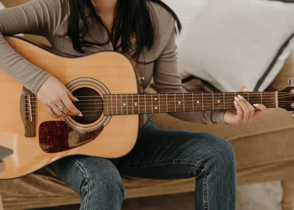 Photo of a Woman in a Brown Long Sleeve Shirt Playing an Acoustic Guitar