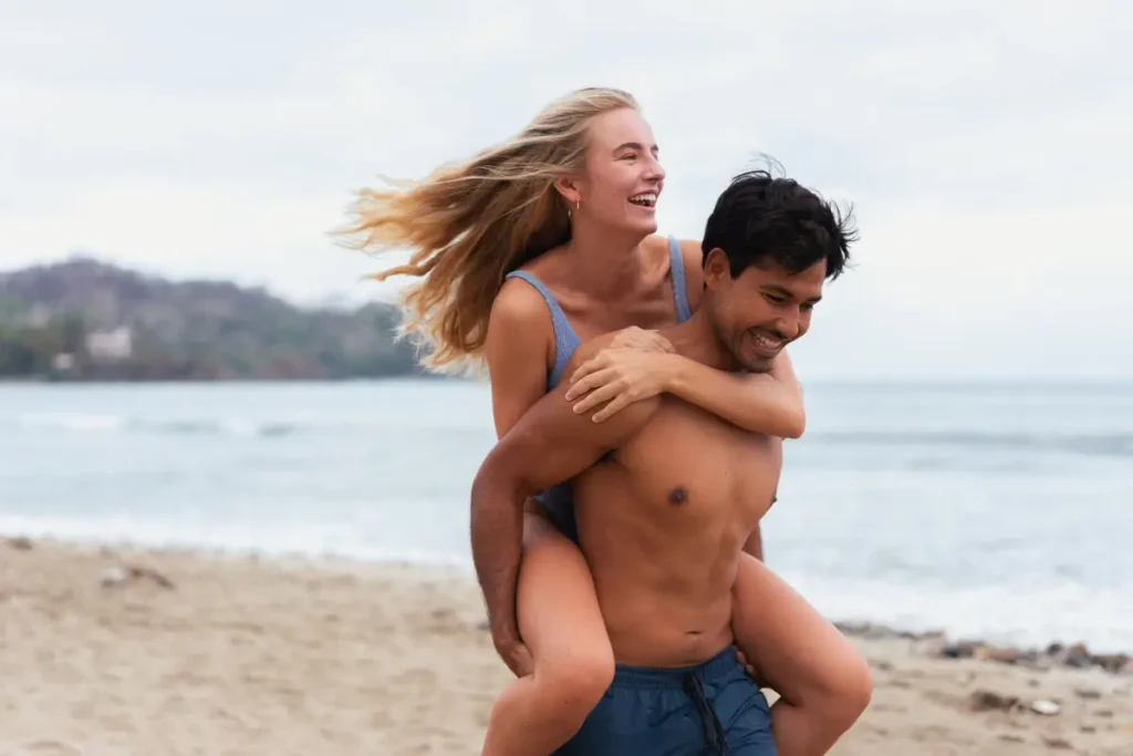 Carefree couple enjoying a playful piggyback ride on a sunny beach day. Beach Captions for Instagram